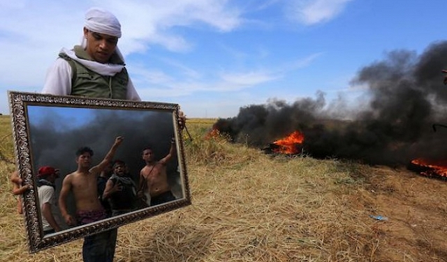 شاب فلسطينيّ يحمل مرآة بالقرب من الشريط الحدودي لغزة