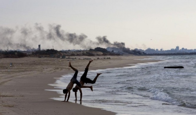 شابان يتدربان على شاطئ غزّة ودخان المظاهرات خلفهما 